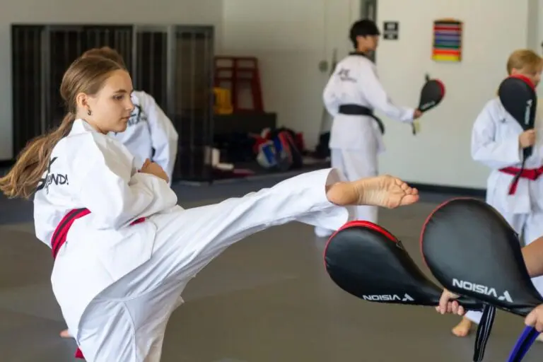 Teen practicing taekwondo kick drills with instructor holding pads