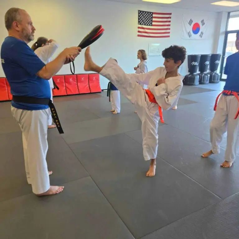Young martial arts student kicking a target pad held by an instructor during dojo class drills martial arts practice habits for beginners